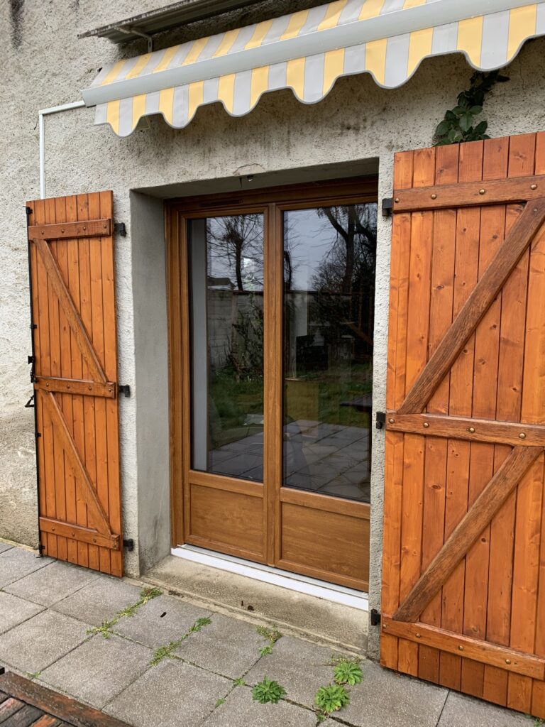 Porte-fenêtre en bois avec volets battants et store banne – Accès direct à la terrasse pour un espace lumineux et chaleureux.