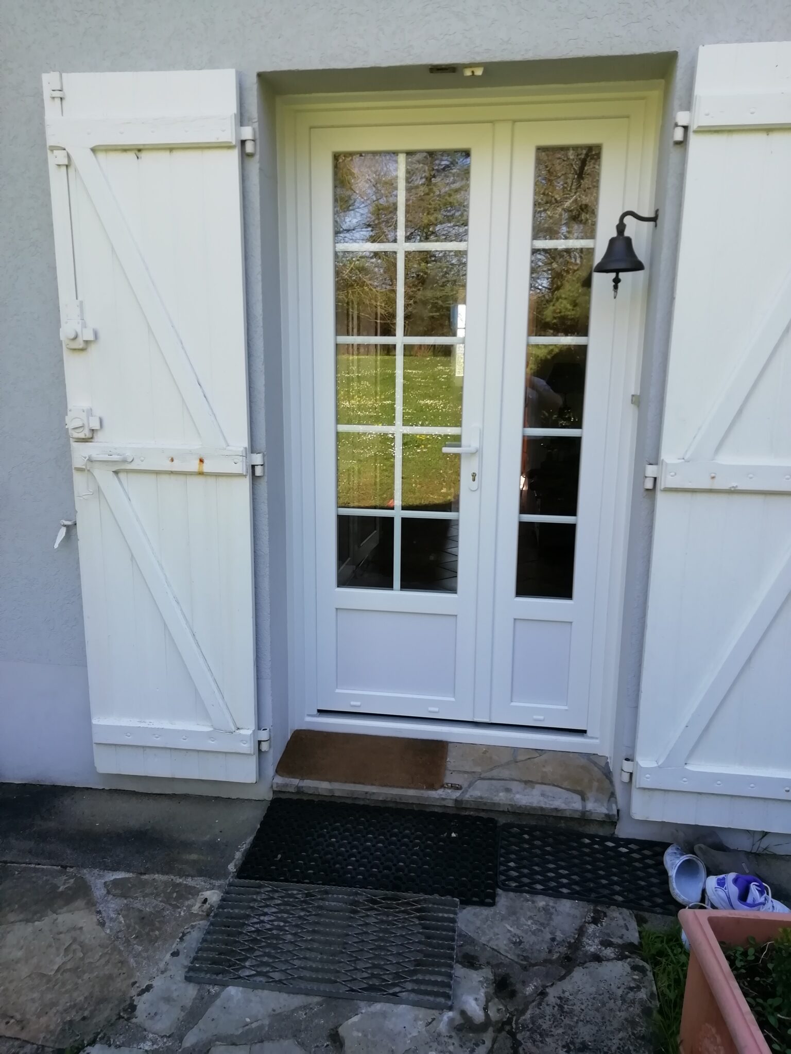 Porte d’entrée vitrée en PVC blanc avec croisillons et volets bois – Sécurité et élégance pour une entrée lumineuse.